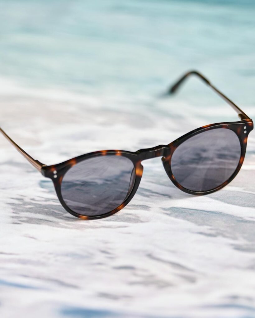 Tortoiseshell sunglasses resting on a sandy beach with ocean waves in the background.